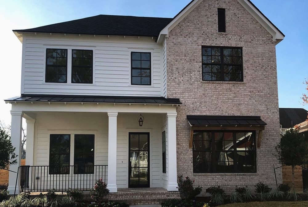 A neutral siding and stone color palette with white siding, red-ish brick and black windows