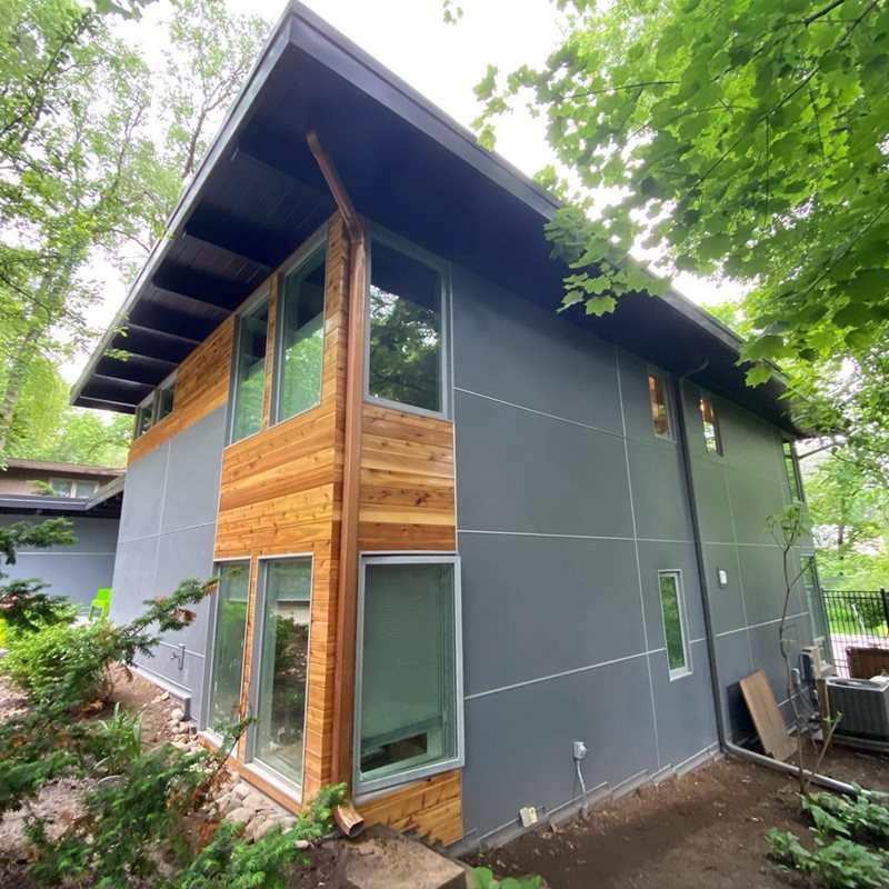 Modern home design with a clean and minimalist exterior, featuring sleek lines, large windows, and a mix of materials including wood siding and stone accents.
