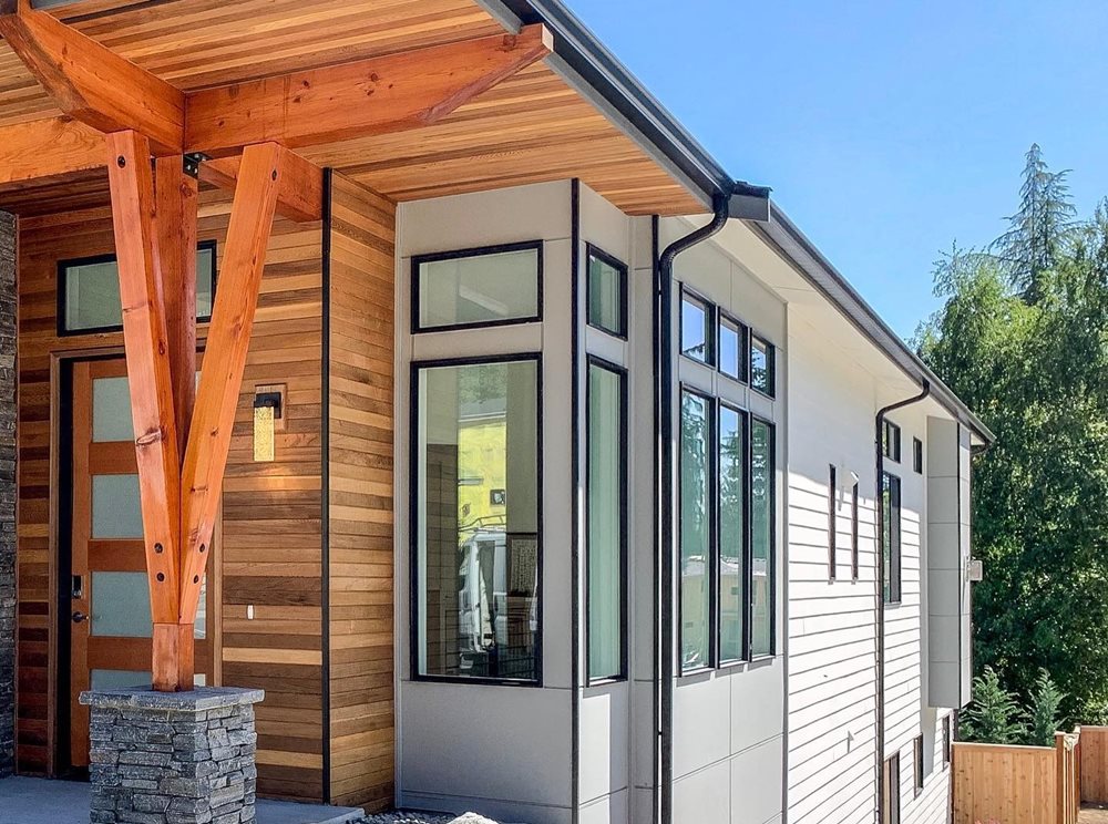Modern home exterior featuring a combination of white, black and wood-colored cladding, flat rooflines, large windows, and clean geometric shapes